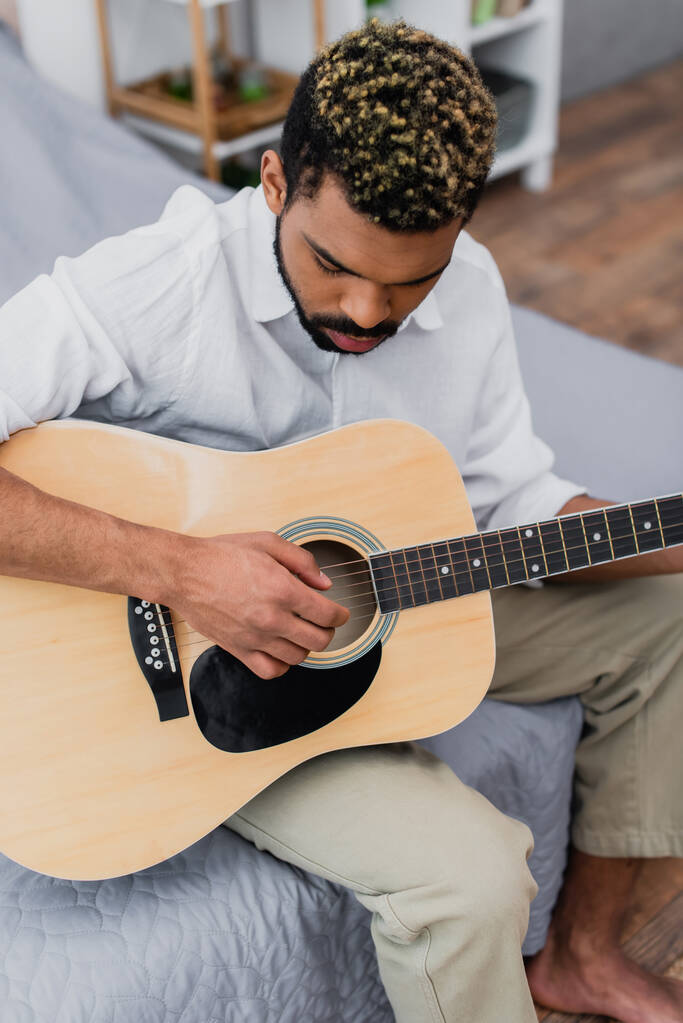 visão de alto ângulo do jovem afro-americano com cabelo tingido tocando guitarra acústica no quarto - Foto, Imagem