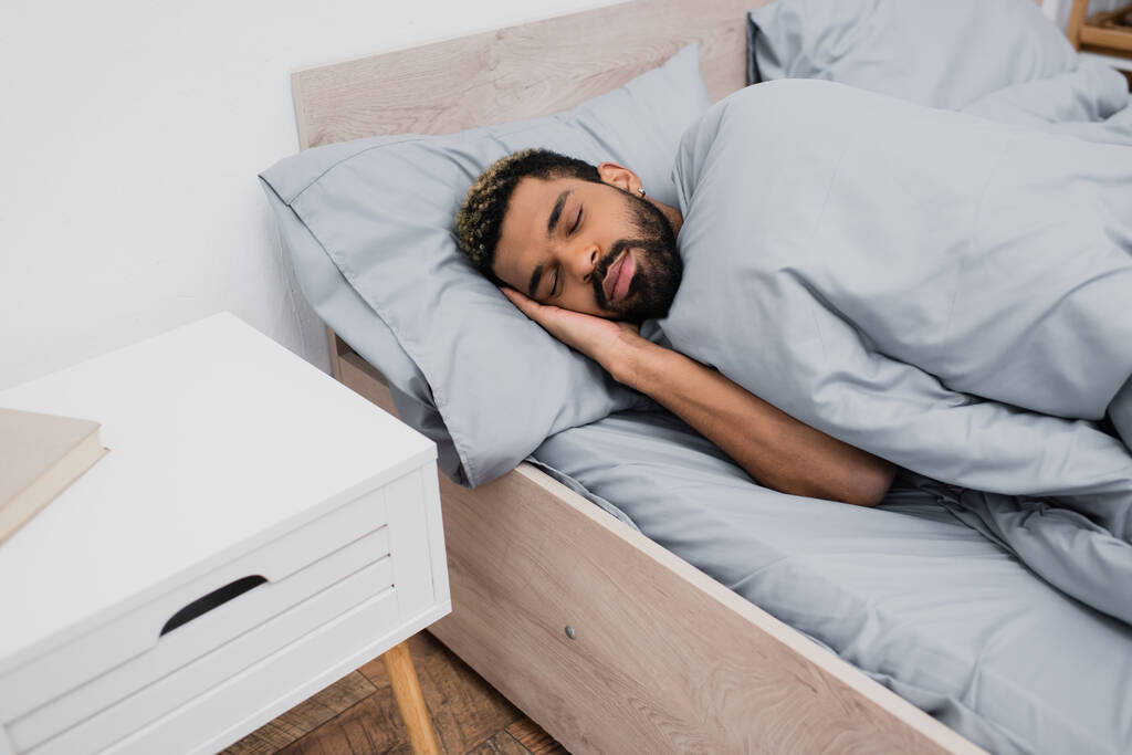 νεαρός Αφροαμερικάνος με κλειστά μάτια κοιμάται στο κρεβάτι - Φωτογραφία, εικόνα