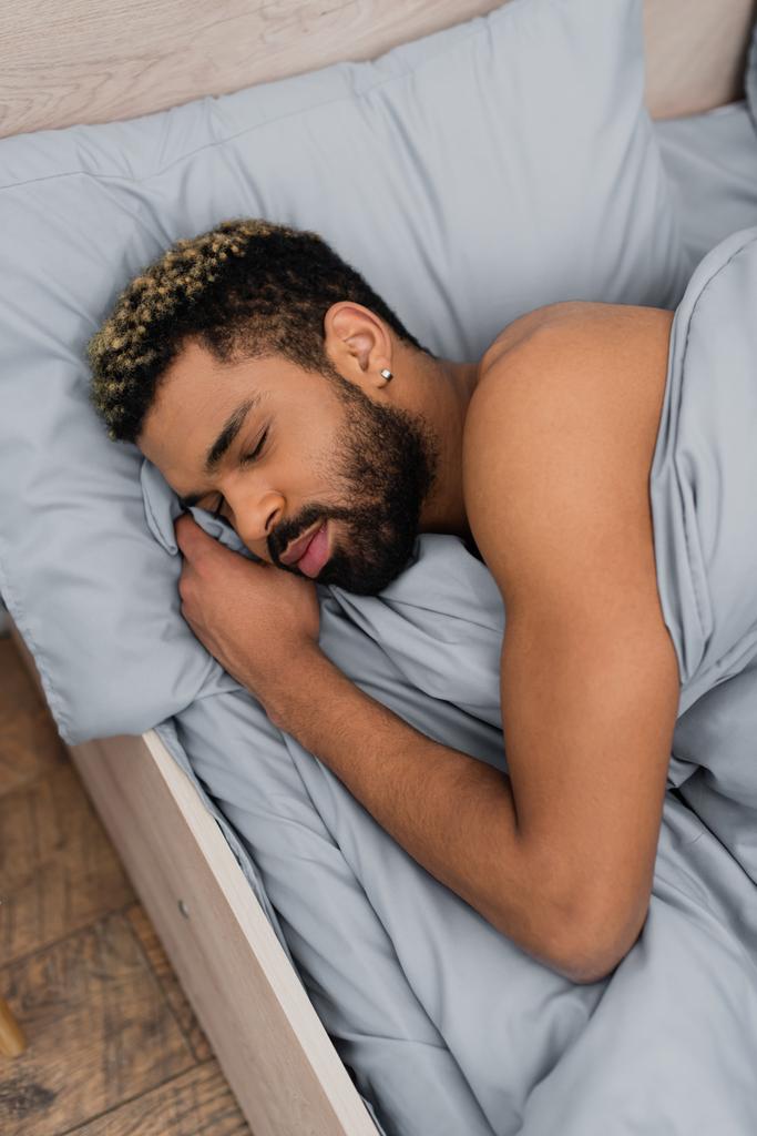 Hochwinkelaufnahme eines bärtigen afrikanisch-amerikanischen Mannes mit geschlossenen Augen, der im Bett schläft - Foto, Bild