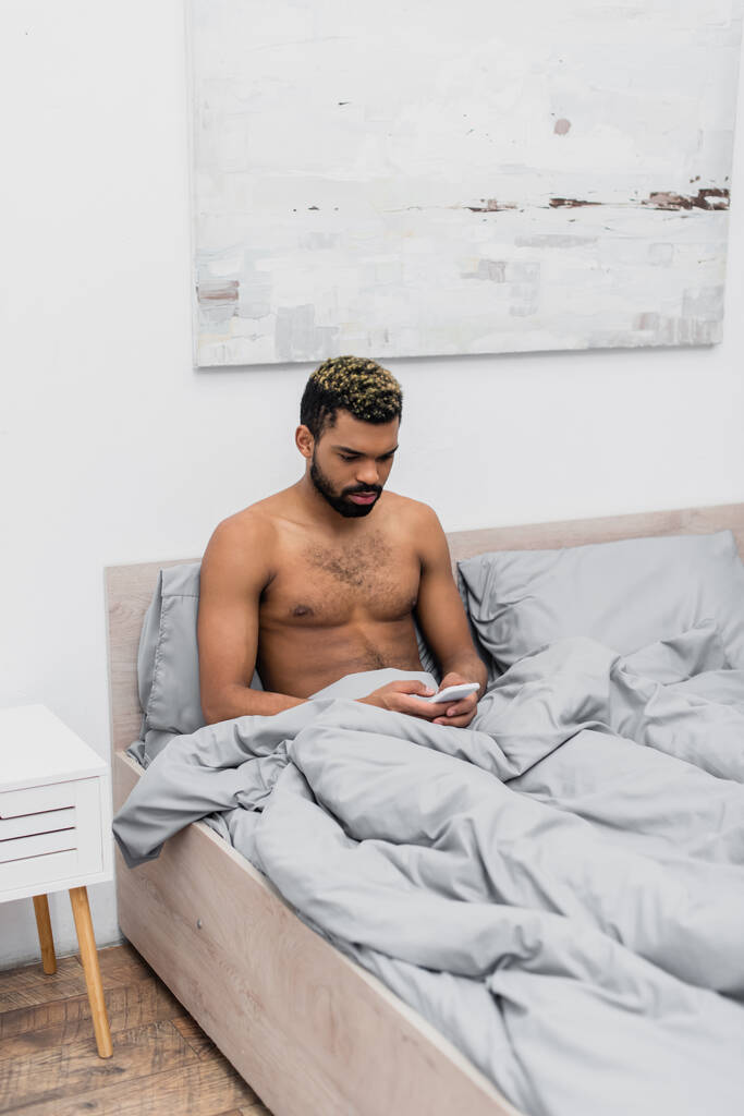 homem americano africano sem camisa com cabelo tingido conversando no telefone celular na cama - Foto, Imagem