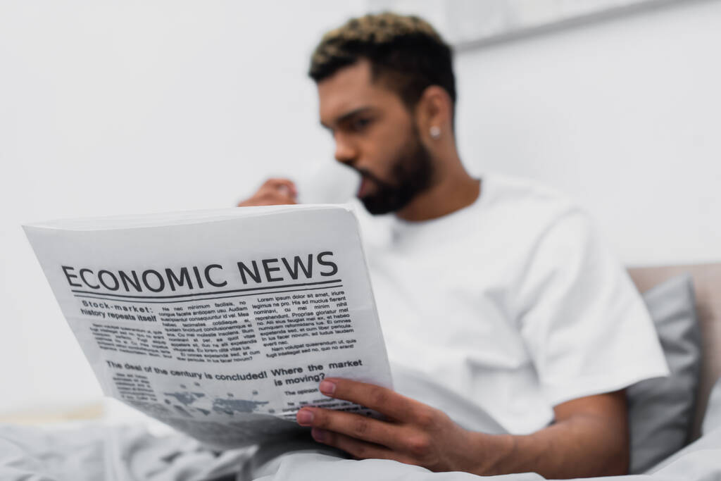 blurred african american man with dyed hair drinking coffee while holding newspaper in bed - Photo, Image