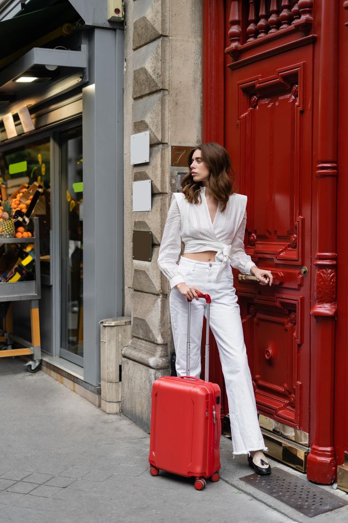 Stylish woman with suitcase standing near building on urban street in Paris  - Photo, Image