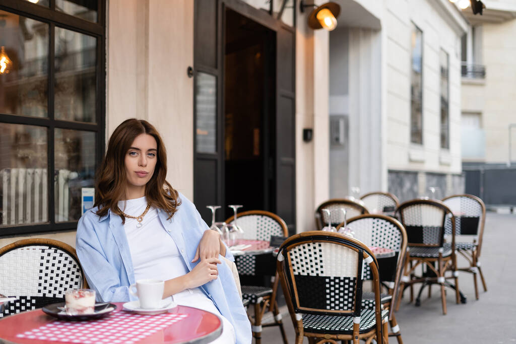 Mulher morena olhando para a câmera perto de café e sobremesa no café ao ar livre em Paris  - Foto, Imagem