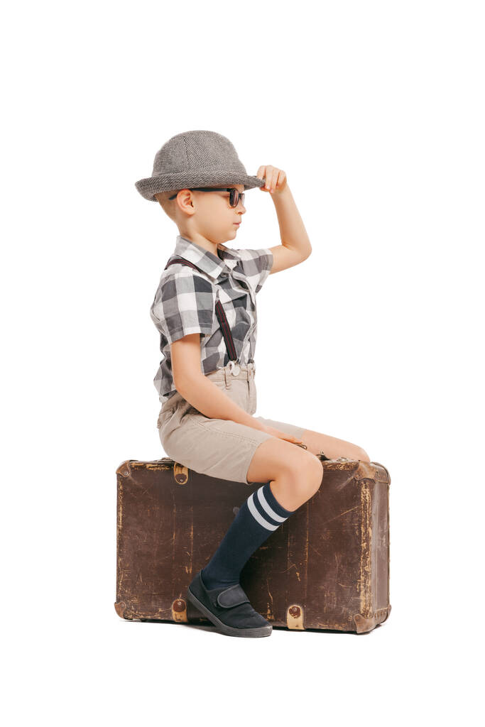 Auf Reisen gehen. Porträt eines netten kleinen Jungen, glücklichen Kindes mit Brille und Hut, das isoliert auf weißem Studiohintergrund auf einem großen Koffer sitzt. Konzept kindlicher Emotionen, Mimik - Foto, Bild