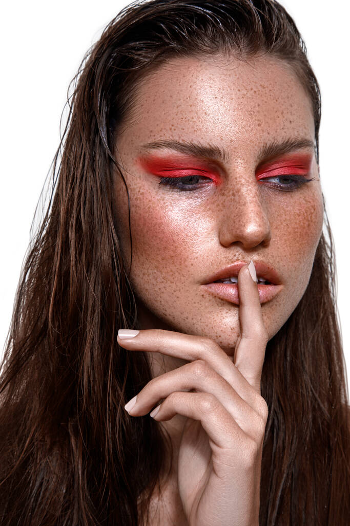 Eine Studioaufnahme einer kaukasischen Frau mit brünetten Haaren und Sommersprossen im Gesicht, die mit dem Finger auf den Lippen posiert - Foto, Bild