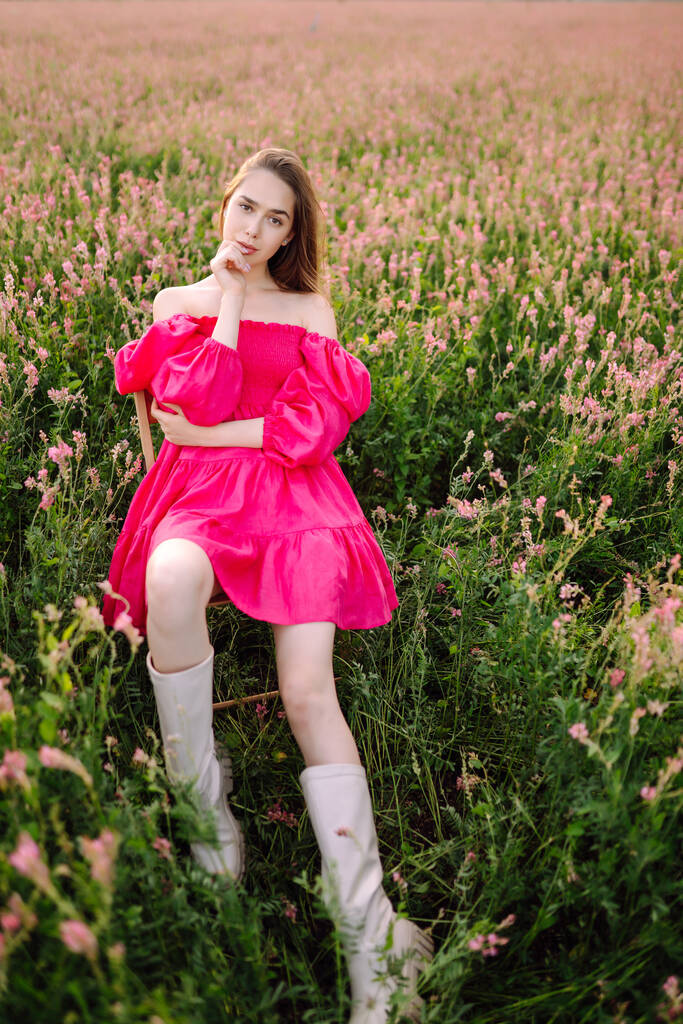 Νεαρή γυναίκα με ροζ φόρεμα στο ανθισμένο χωράφι. Θερινό τοπίο. Μόδα, στυλ έννοια. - Φωτογραφία, εικόνα