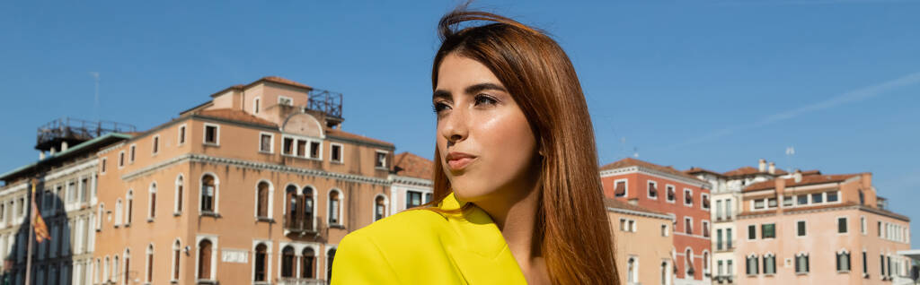jonge roodharige vrouw kijkt weg in de buurt van Venetiaanse gebouwen op de achtergrond, banner - Foto, afbeelding