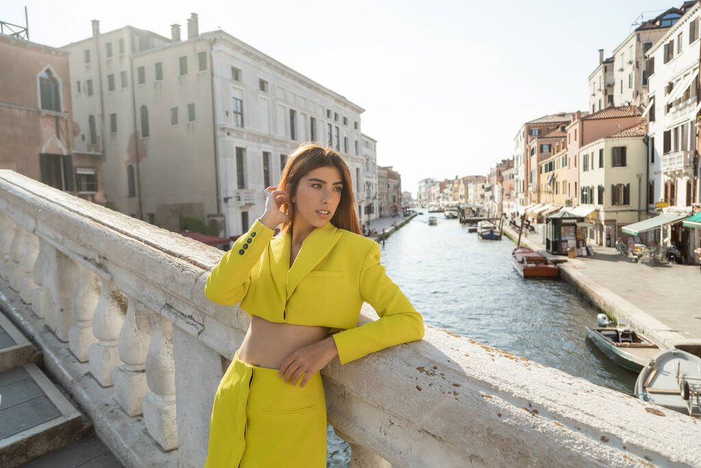 młoda kobieta w żółtych modnych ubraniach naprawianie rudych włosów na moście nad Canal Grande w Wenecji - Zdjęcie, obraz