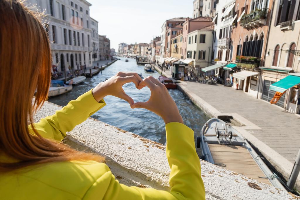 partial view of redhead woman showing heart sign over blurred Grand Canal in Venice - Photo, Image