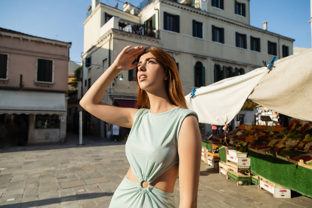 elegant woman with hand above eyes looking away on venetian street near food market - Photo, Image