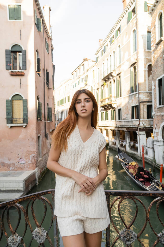 mulher no jumper sem mangas olhando para a câmera perto de cerca sobre o canal veneziano - Foto, Imagem