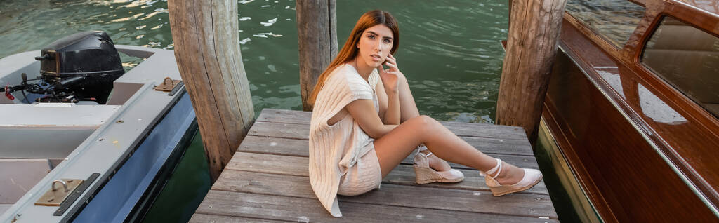 high angle view of young woman sitting on wooden pier near motor boats in Venice, banner - 写真・画像