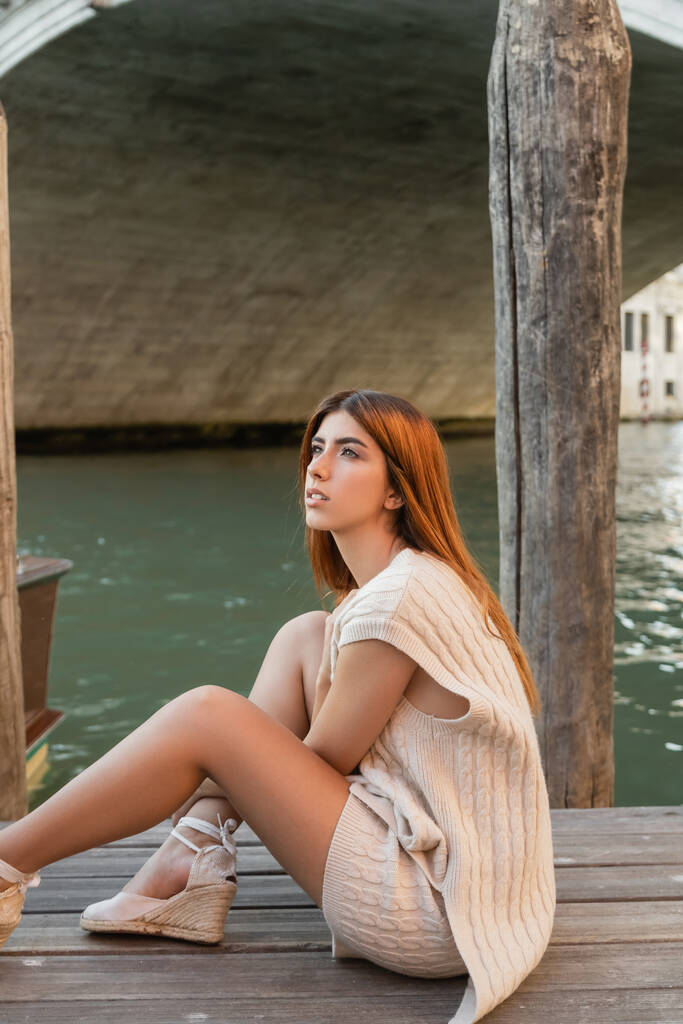 álmodozó vörös hajú nő ül a mólón Velencében, és félrenéz - Fotó, kép