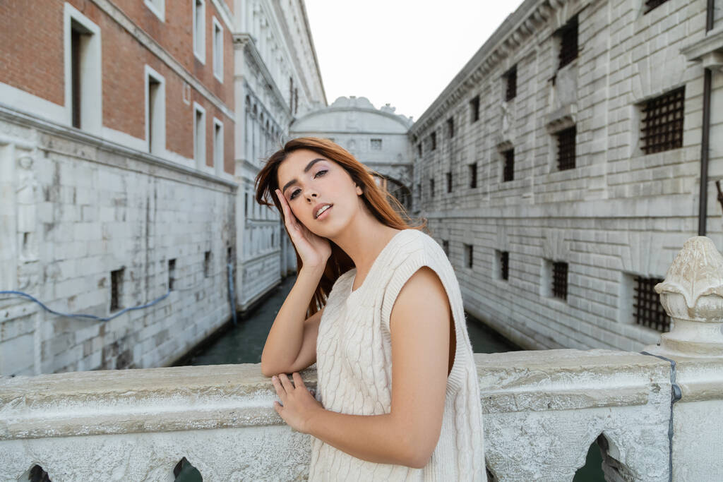 young woman with hand near fence looking at camera near medieval prison in Venice - Photo, Image