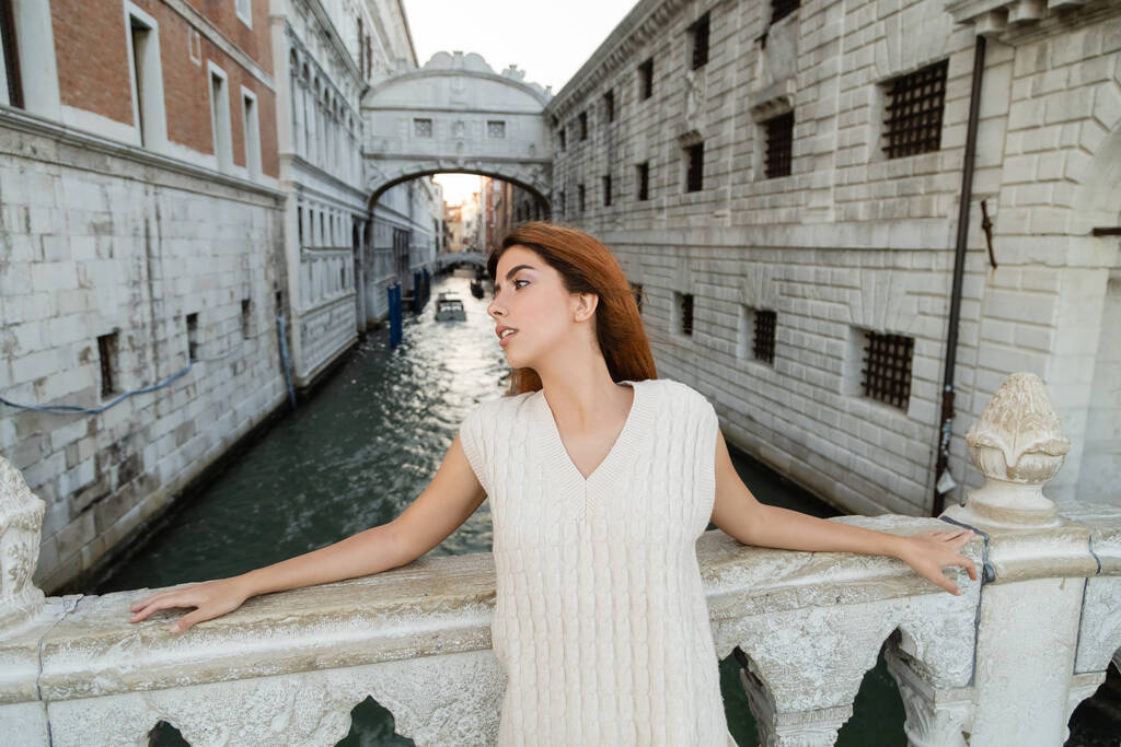 Рудоволоса жінка, що дивиться у далечінь біля мосту Сігс на задньому плані у Венеції. - Фото, зображення