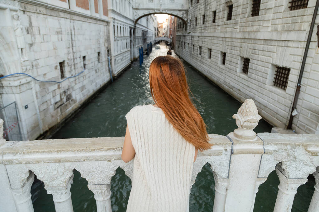 achteraanzicht van roodharige vrouw op brug nabij middeleeuwse gevangenis in Venetië - Foto, afbeelding