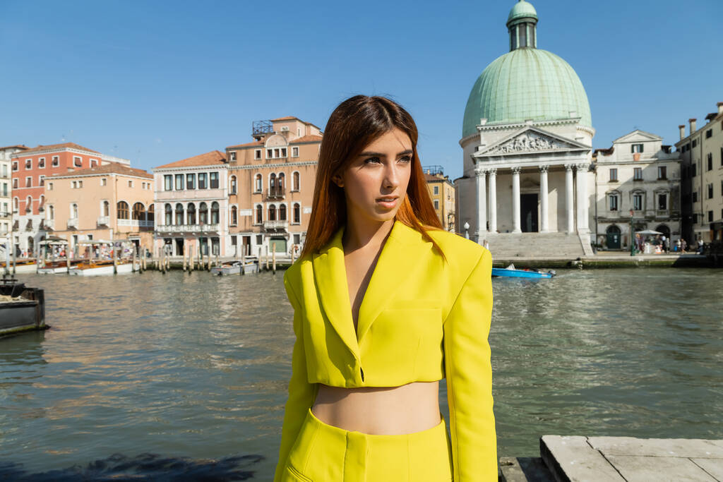 Рыжая женщина в жёлтой куртке смотрит в сторону Большого канала в Венеции - Фото, изображение
