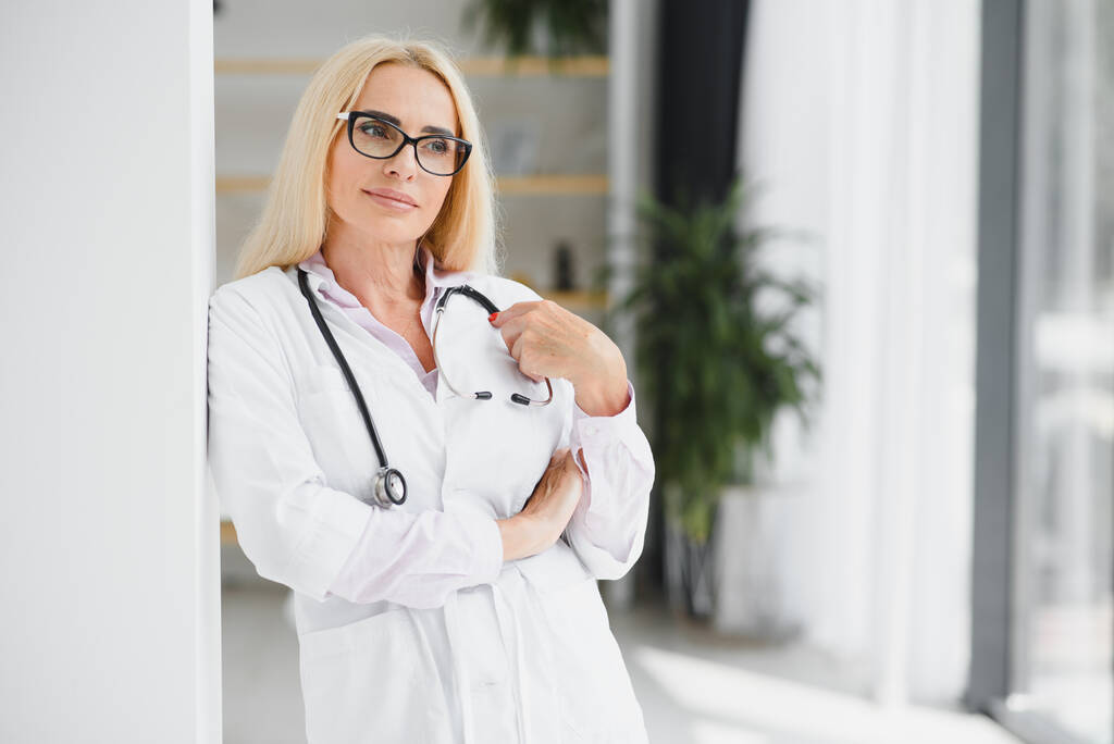 Középkorú női orvos portréja fehér orvosi kabátot visel, sztetoszkóppal a nyakában. Mosolygó orvos áll a magánklinikán. - Fotó, kép