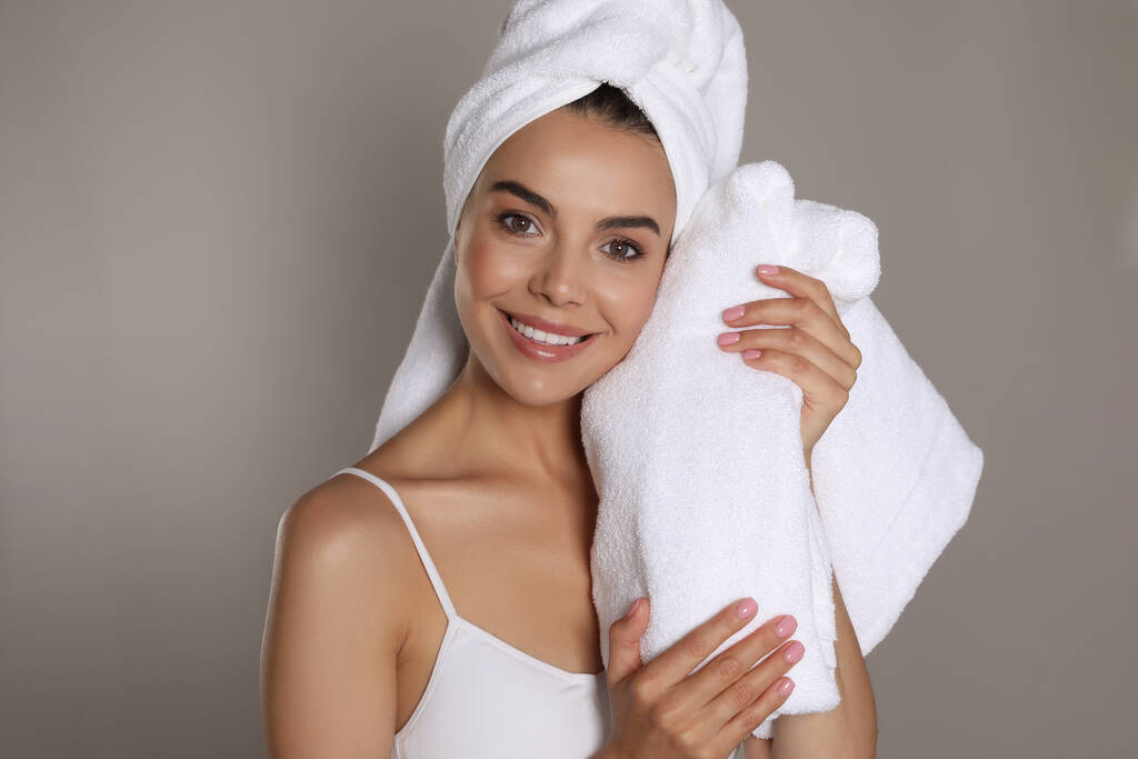 Krásná mladá žena s ručníky na šedém pozadí - Fotografie, Obrázek