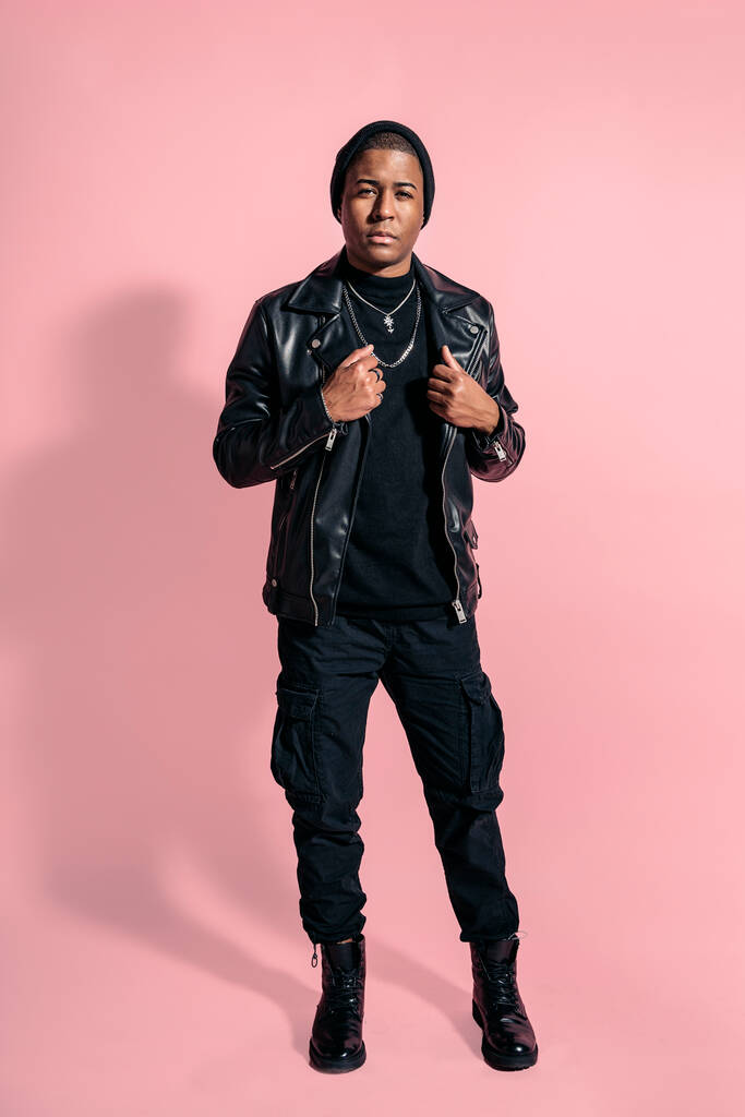 Стокове фото молодого чорношкірого чоловіка в загальному чорному вигляді позує в студійному кадрі на рожевому фоні
. - Фото, зображення