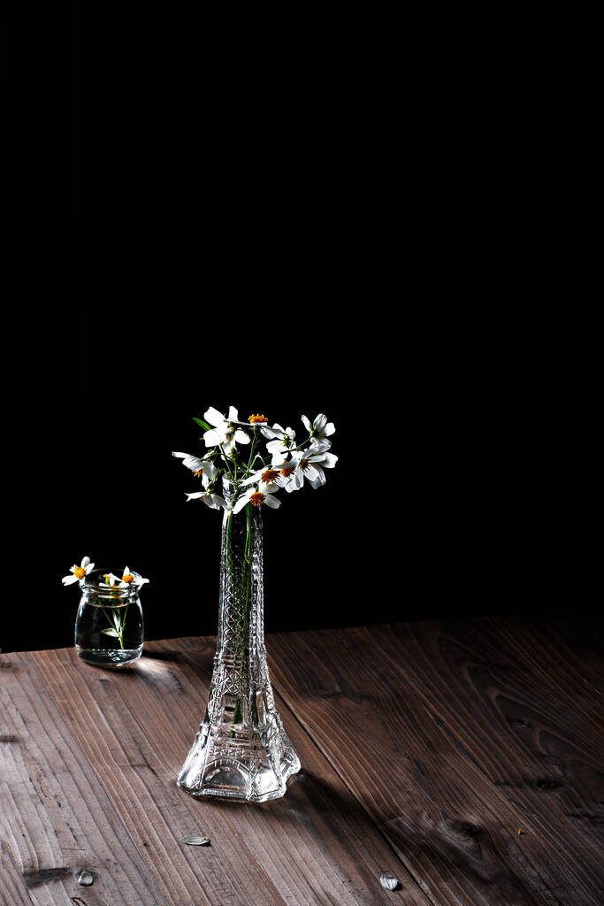 Eine vertikale Nahaufnahme transparenter Blumenvasen auf einem Holztisch vor dunklem Hintergrund - Foto, Bild