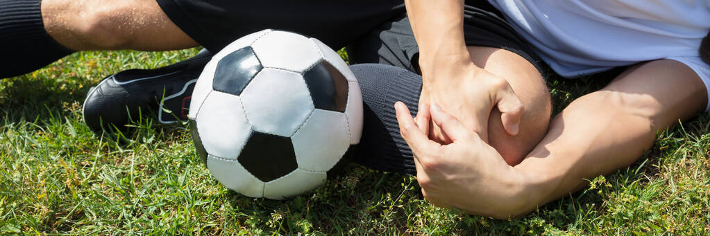 Nahaufnahme eines Fußballers mit Knieverletzung, der auf dem Feld liegt - Foto, Bild