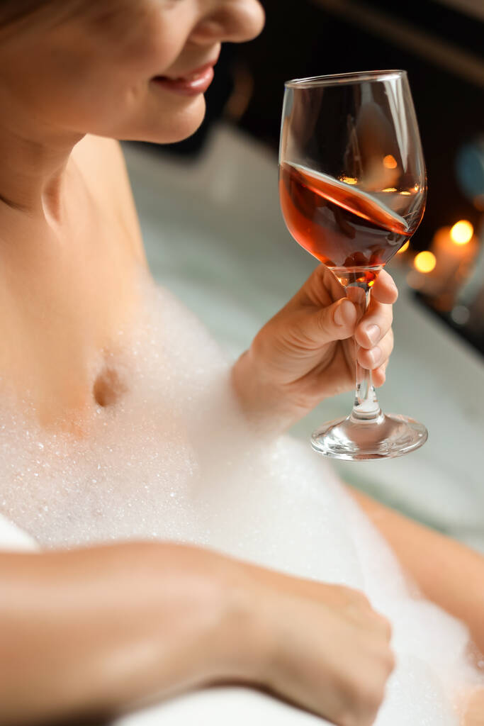 Kobieta pijąca wino podczas kąpieli z bąbelkami, zbliżenie. Romantyczna atmosfera - Zdjęcie, obraz