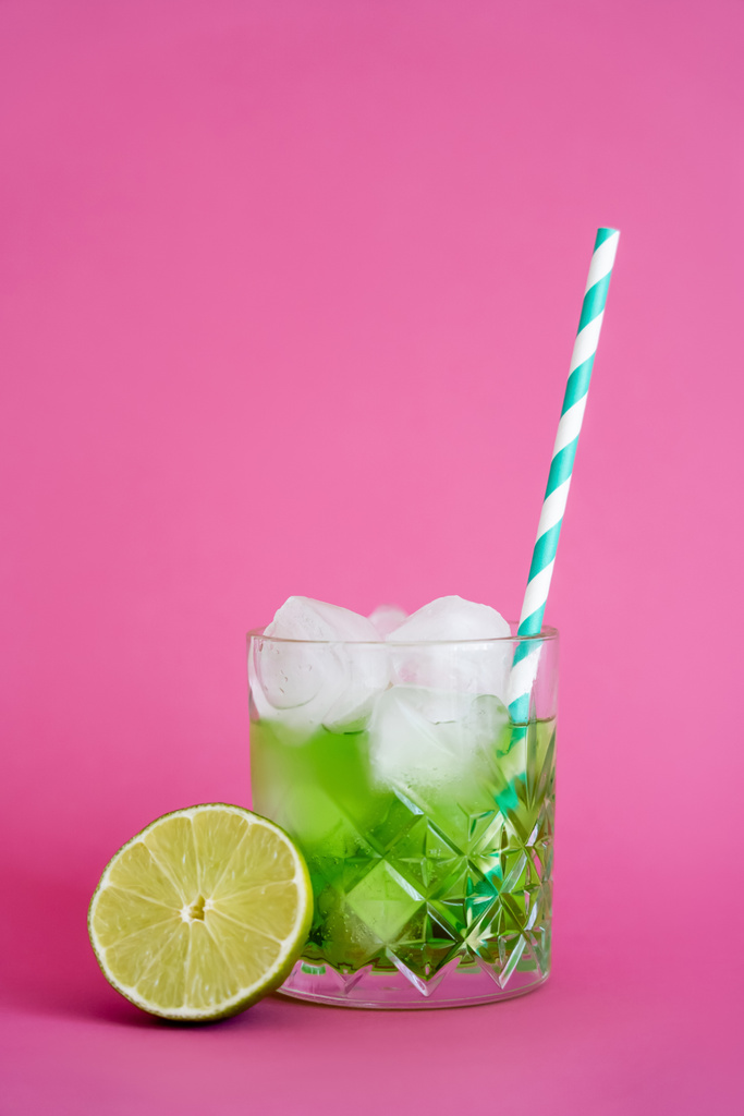 κατεψυγμένα παγάκια σε ποτήρι με πράσινο ποτό μοχίτο κοντά σε φέτες ασβέστη σε ροζ  - Φωτογραφία, εικόνα
