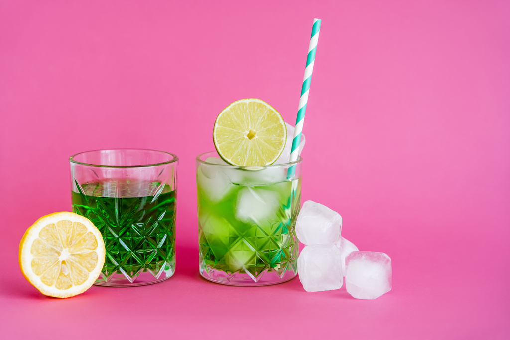 ice cubes in glass with mojito near green beverage and limes on pink  - Foto, Bild