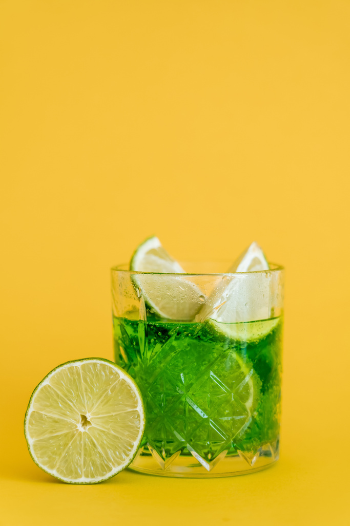 sliced limes in glass with sparkling mojito drink on yellow  - Foto, imagen