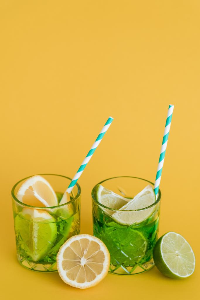 sliced citrus fruits in glasses with sparkling mojito drink and straws on yellow  - Photo, Image