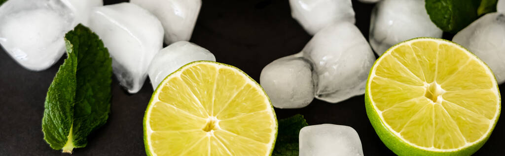 high angle view of melting ice cubes near sliced limes and milt leaf on black background, banner - Photo, Image