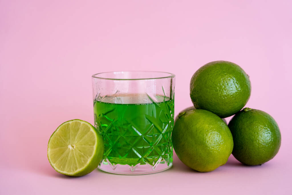 limas frescas verdes perto de bebida alcoólica em vidro facetado em rosa - Foto, Imagem