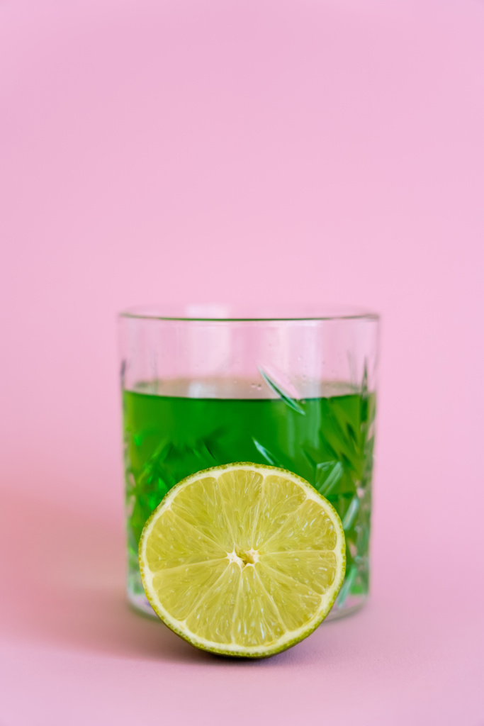 grüne frische Limette in der Nähe von Alkohol im Glas auf rosa - Foto, Bild