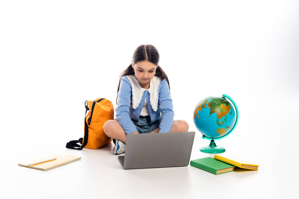 Schoolkid using laptop near books and globe on white background - Photo, Image