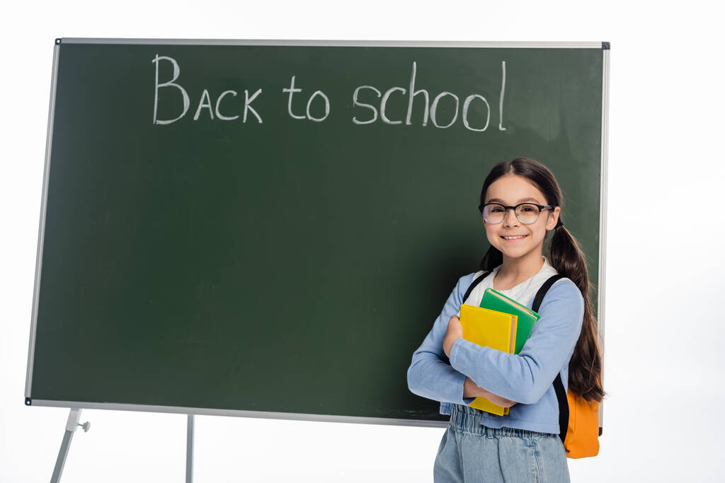 Fröhliches Schulkind mit Büchern in der Nähe von Kreidetafeln mit Schulbuchstaben auf weißem Hintergrund  - Foto, Bild