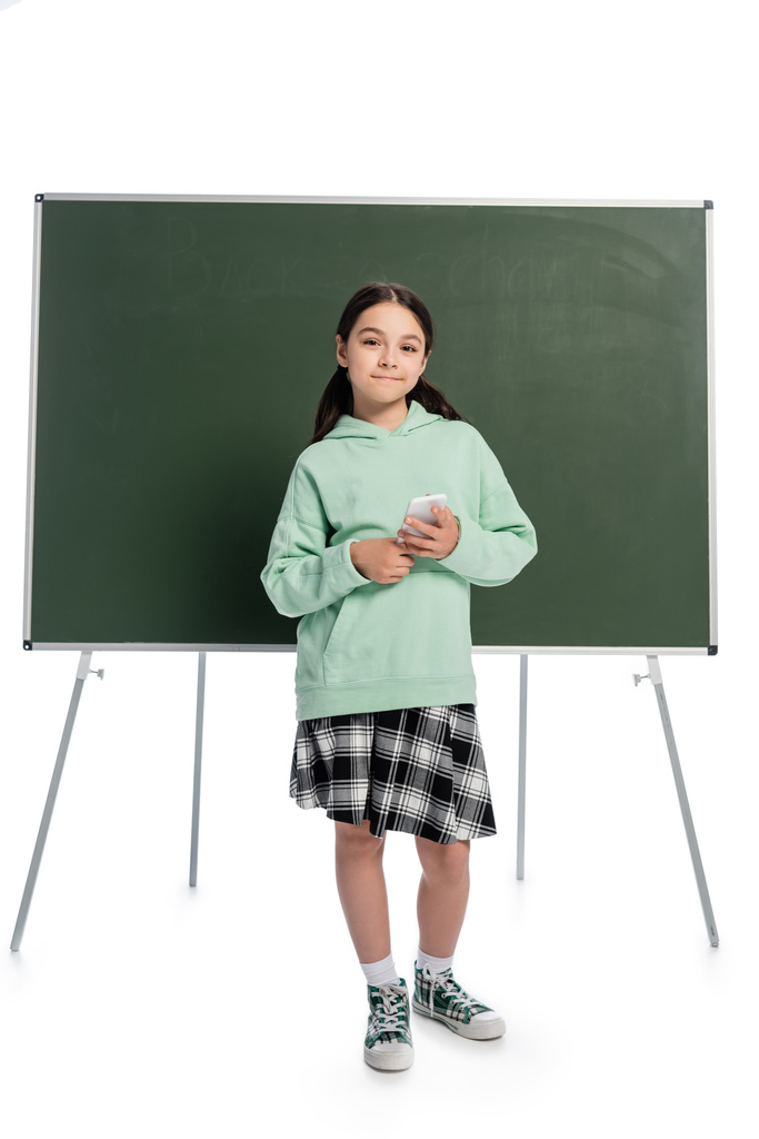 Πλήρες μήκος της μαθήτριας κρατώντας smartphone κοντά στο chalkboard σε λευκό φόντο - Φωτογραφία, εικόνα