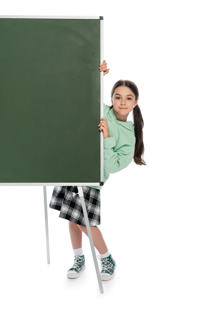 Полная длина улыбающейся школьницы, стоящей рядом с доской на белом фоне  - Фото, изображение