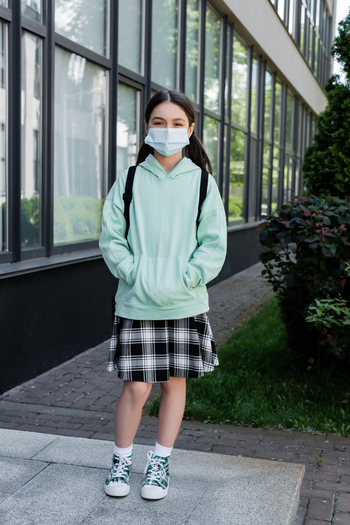 Schoolchild in medical mask standing near building on urban street  - Photo, Image