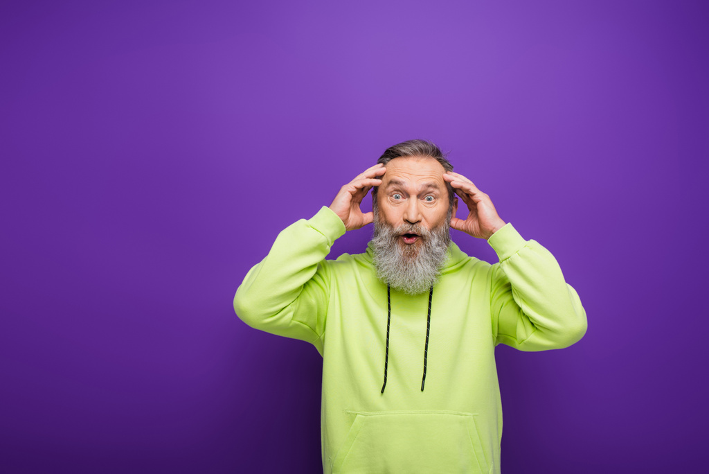 shocked and bearded senior man with grey hair looking at camera on purple  - Photo, Image