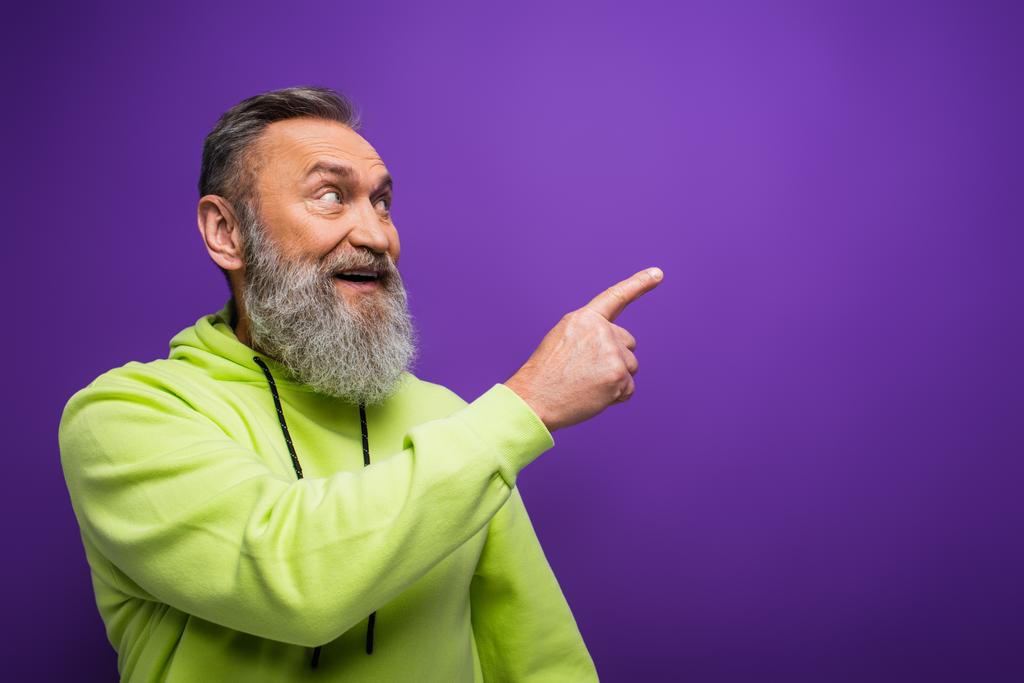 весёлый пожилой мужчина с бородой и седыми волосами, указывающими пальцем на фиолетовый - Фото, изображение