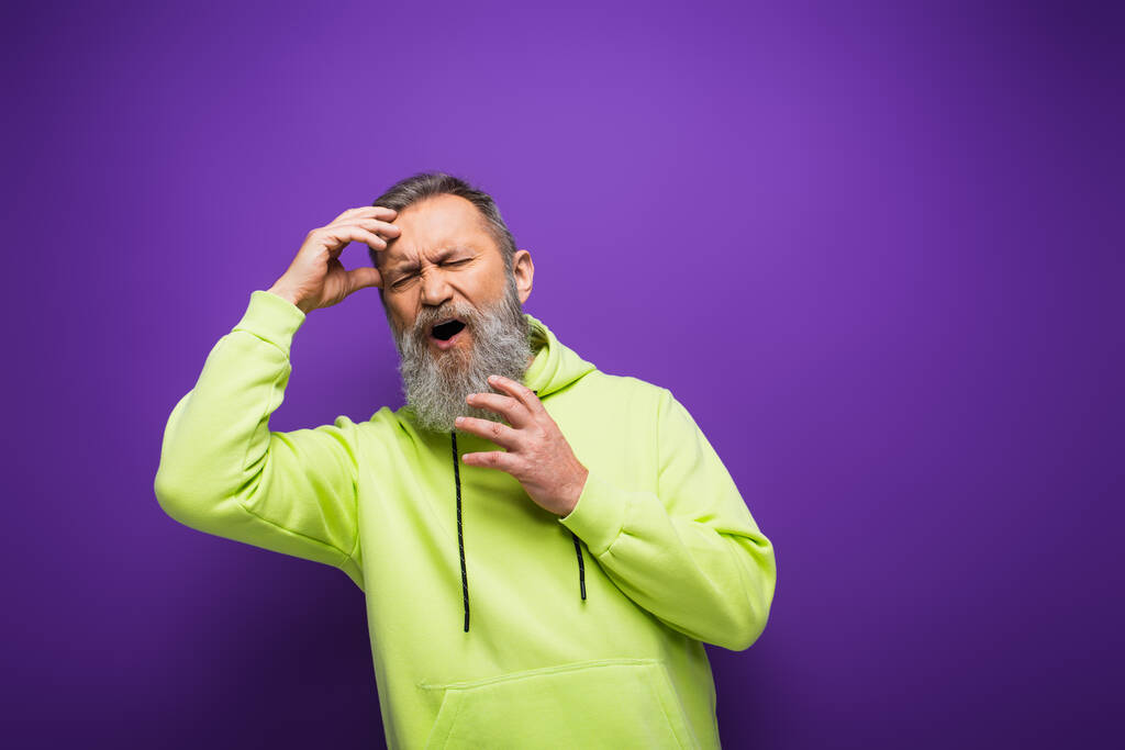 старший мужчина с бородой и седыми волосами с головной болью на фиолетовом фоне  - Фото, изображение