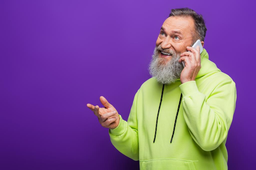 szczęśliwy senior z brodą i siwymi włosami rozmawiający na smartfonie na fioletowym  - Zdjęcie, obraz