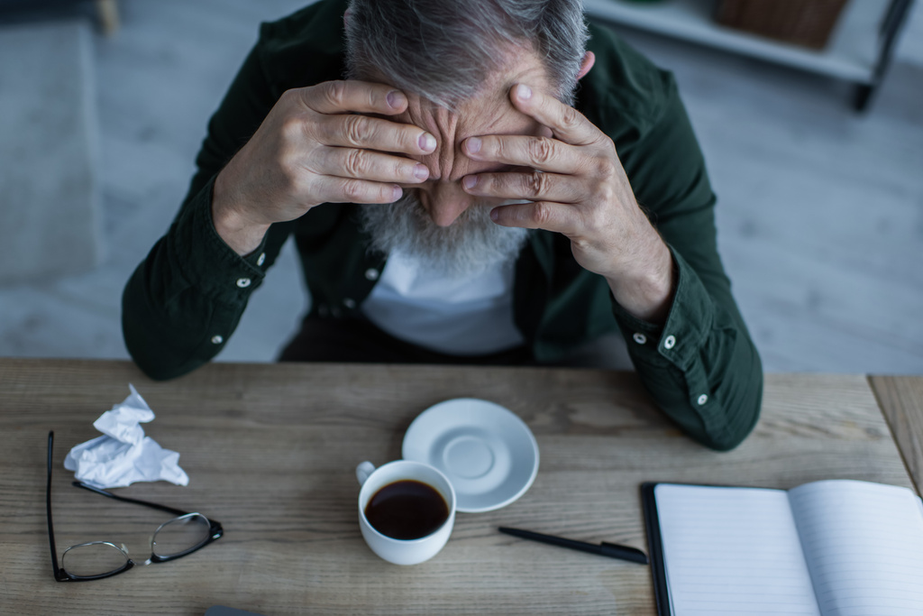 vysoký úhel pohledu nešťastného staršího muže opírající se o stůl s šálkem kávy a papírnictví  - Fotografie, Obrázek