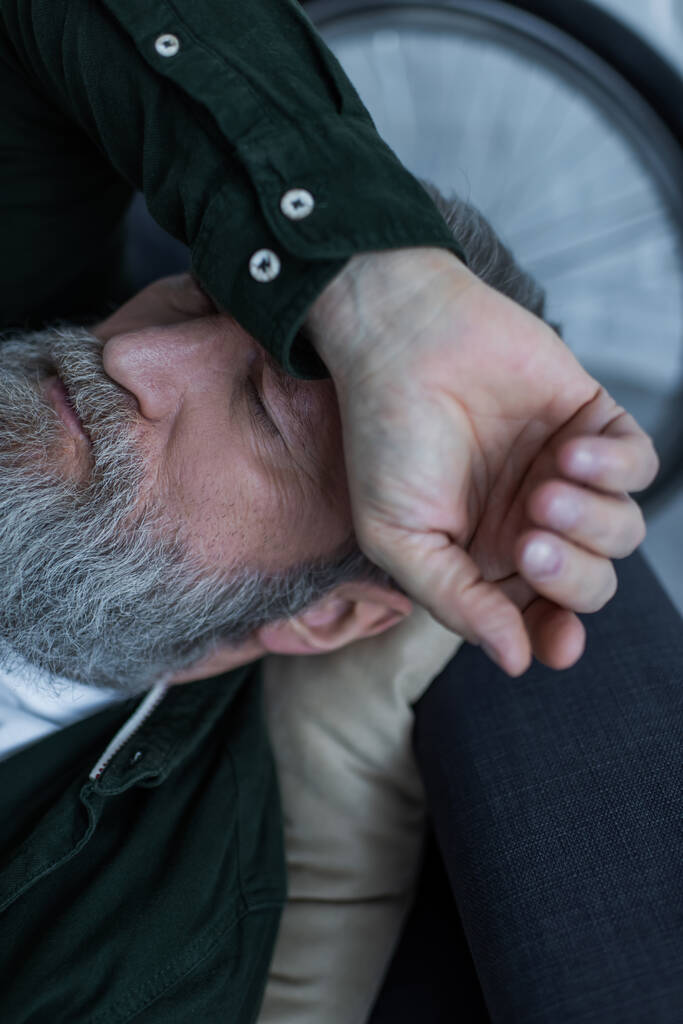 vrchol pohled na nešťastný starší muž s vousy ležící na gauči při utrpení krize  - Fotografie, Obrázek