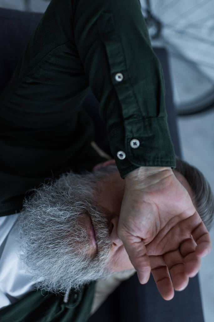 vista superior de un hombre jubilado infeliz con barba tumbado en el sofá mientras sufre una crisis  - Foto, Imagen
