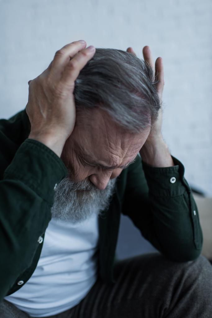 stressed senior man with beard touching head while suffering from headache at home - Photo, Image