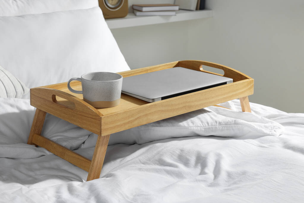 Wooden tray with modern laptop and cup of aromatic drink on bed indoors - Photo, Image