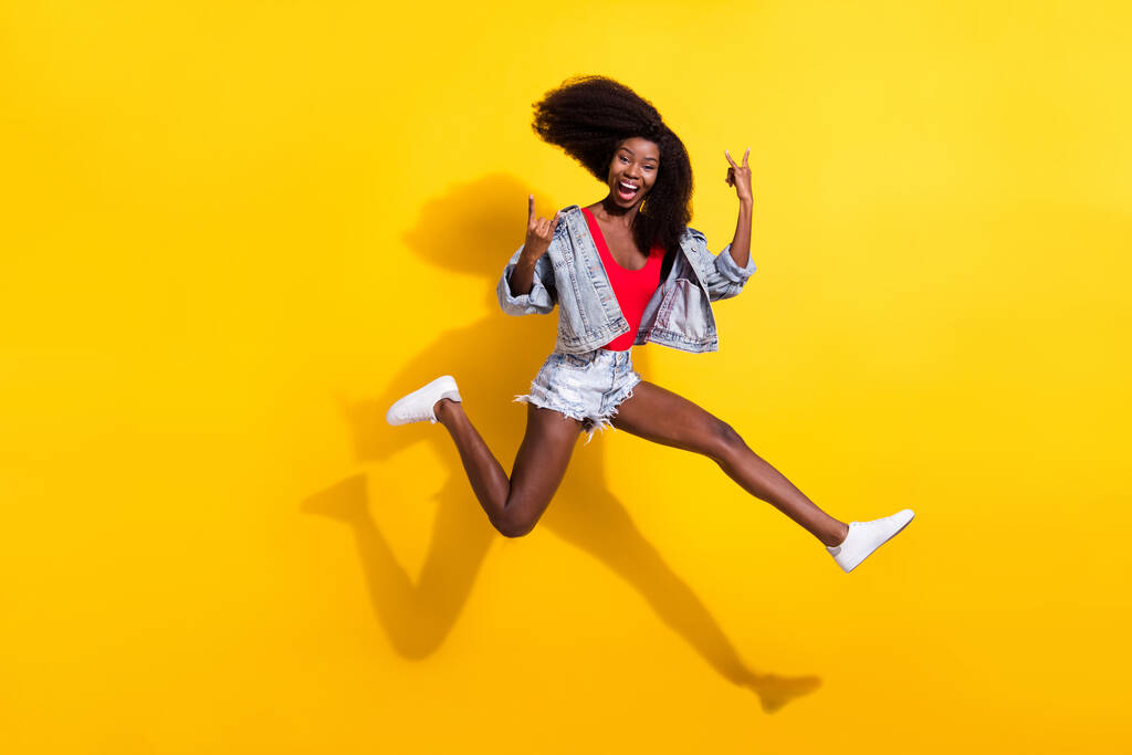 Ganzkörpergröße Foto von Mädchen springen zeigt Schwermetall Zeichen lachen isoliert helle gelbe Farbe Hintergrund. - Foto, Bild