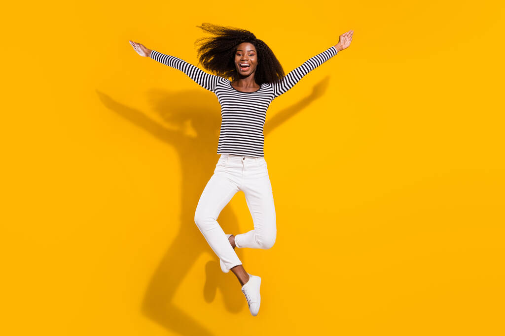 Полная длина тела фото женщина прыгает вверх смеясь небрежно в полосатой рубашке изолированы яркий желтый цвет фона. - Фото, изображение